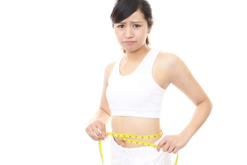 不満げにメジャーで腹囲を測る女性の画像