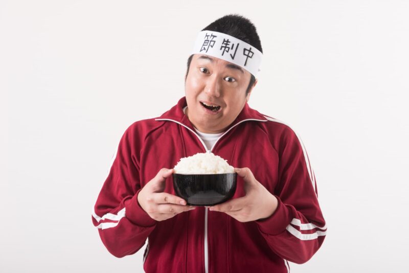 ごはん茶碗を持って笑顔の男性（赤ジャージ・ハチマキ）