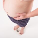 お腹を抱えながら体重計に乗る男性の画像