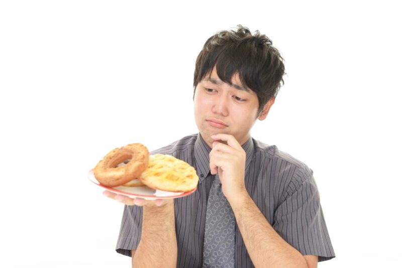 ドーナツを見つめて悩んでいる男性の画像
